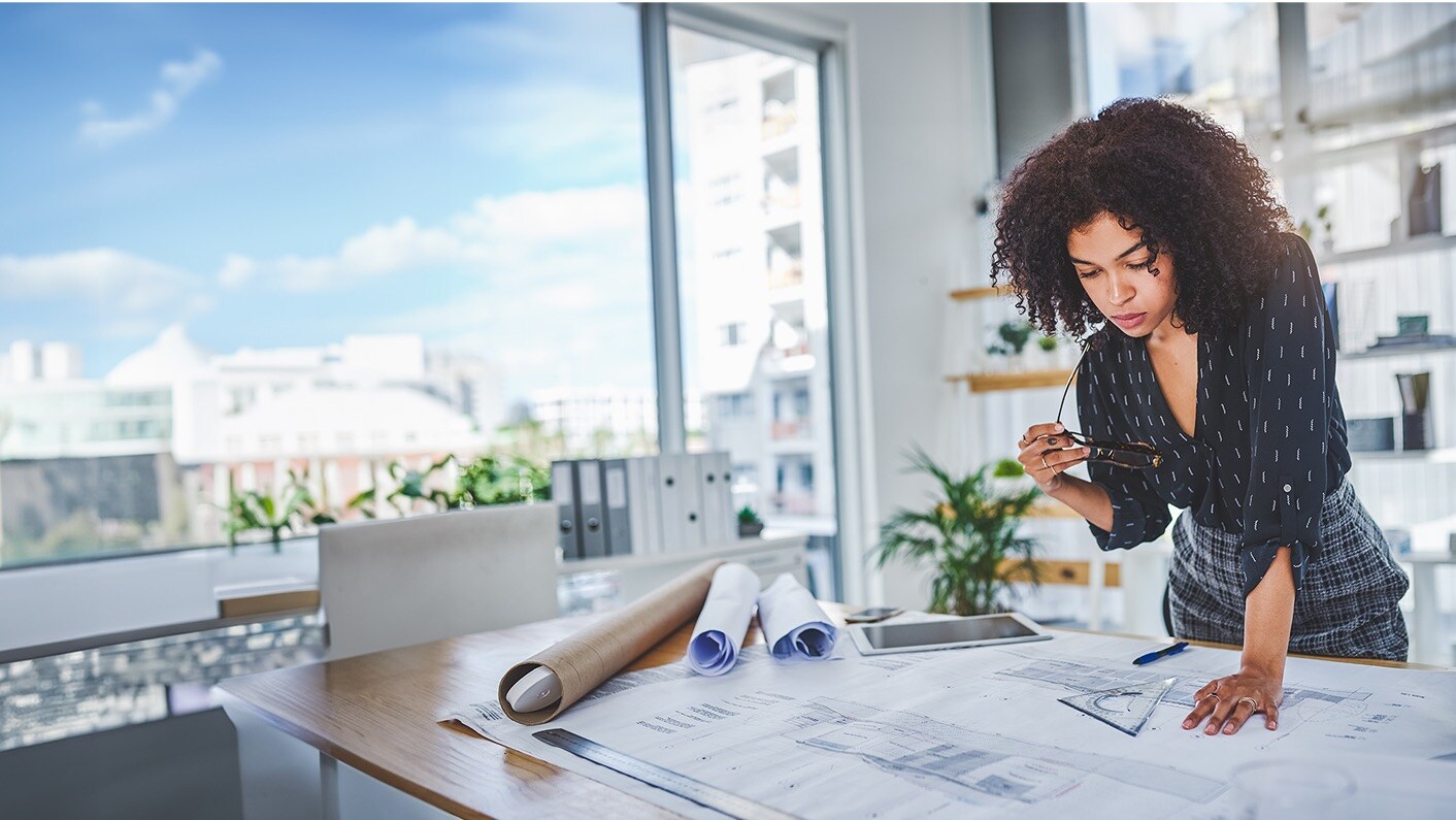 A female architect examining blueprints on a desk in a modern office.